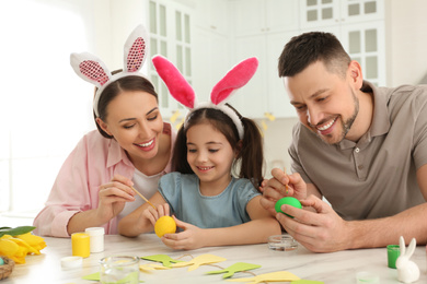Happy father, mother and daughter painting Easter eggs at table in kitchen