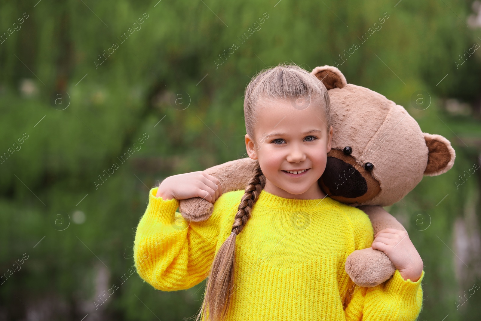 Photo of Cute little girl with teddy bear outdoors. Space for text