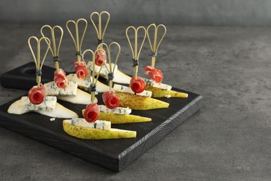 Photo of Tasty canapes with pears, blue cheese and prosciutto on grey table, closeup. Space for text