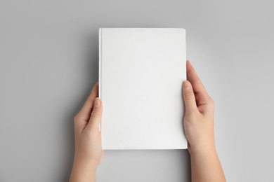 Photo of Woman holding book with blank cover on grey background, top view