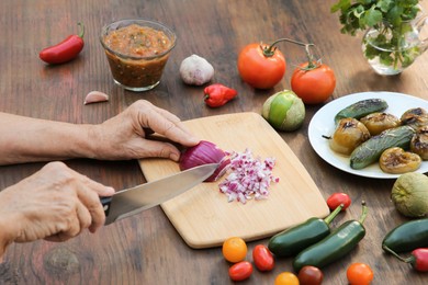 Photo of Woman cutting red onion for salsa sauce at wooden table, closeup