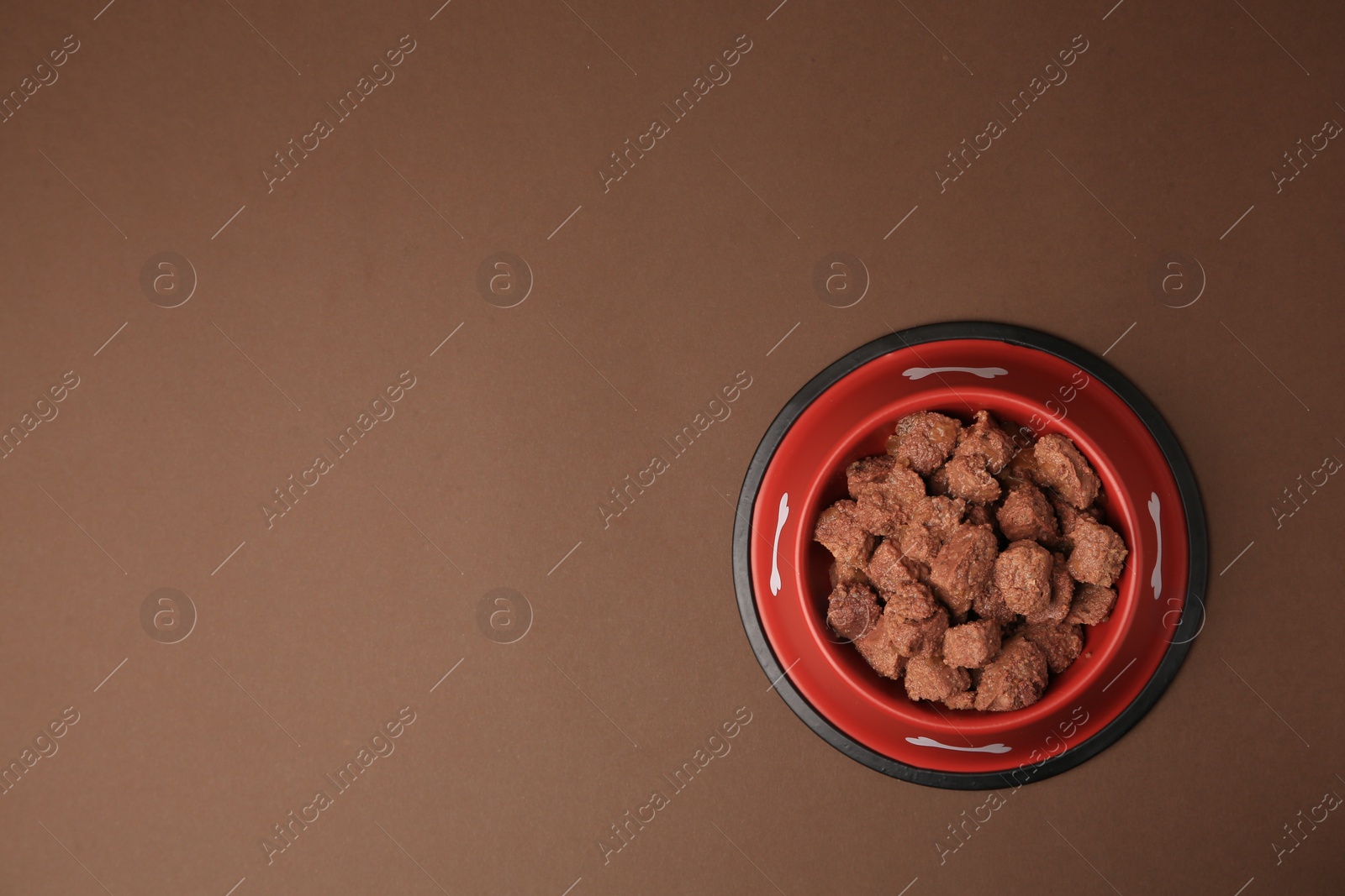 Photo of Wet pet food in feeding bowl on brown background, top view. Space for text