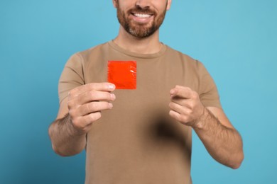 Man holding condom on light blue background, closeup. Safe sex