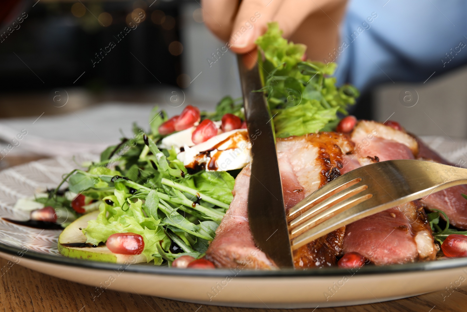 Photo of Woman eating delicious salad with roasted duck breast at wooden table, closeup