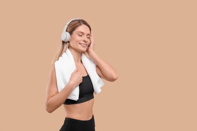 Photo of Athletic woman with headphones and white towel on beige background, space for text