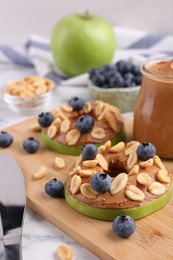 Photo of Slices of fresh apple with peanut butter, blueberries and nuts on white marble table