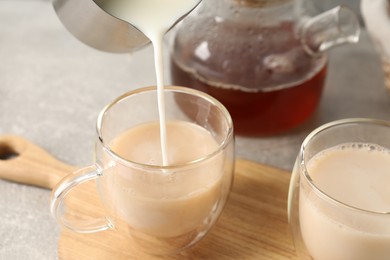 Photo of Pouring milk into glass cup with tea at light grey table, closeup