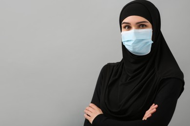 Portrait of Muslim woman in hijab and medical mask on light gray background, space for text