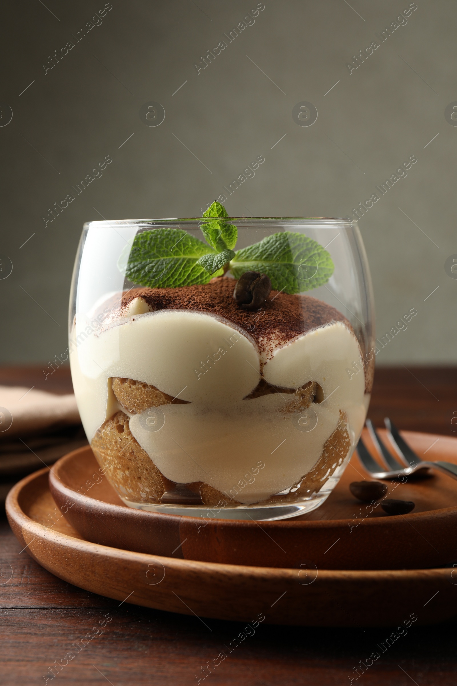 Photo of Delicious tiramisu in glass, mint leaves, coffee beans and fork on wooden table