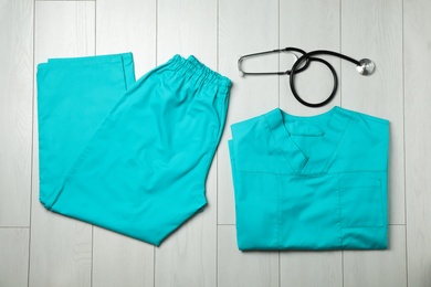 Clean scrubs and stethoscope on wooden background, top view. Medical objects