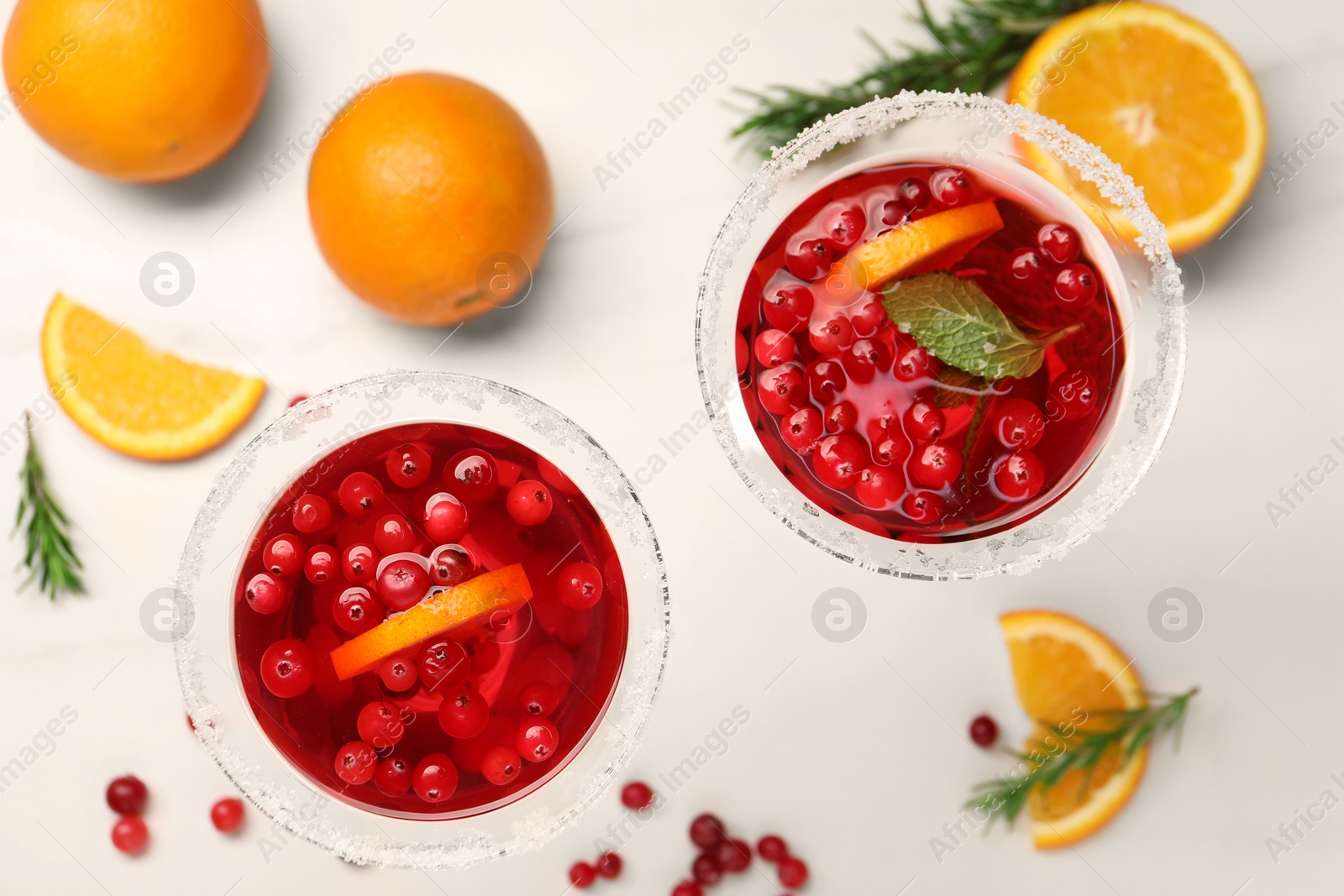 Photo of Tasty cranberry cocktail in glasses, rosemary and oranges on white table, flat lay