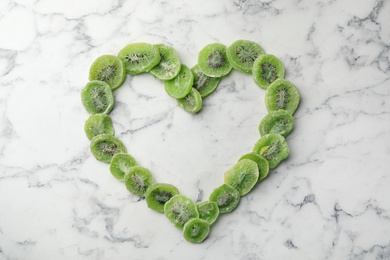 Photo of Heart shaped frame made of kiwi on marble background, top view with space for text. Dried fruit as healthy food