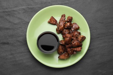 Photo of Tasty roasted meat served with soy sauce on black table, top view