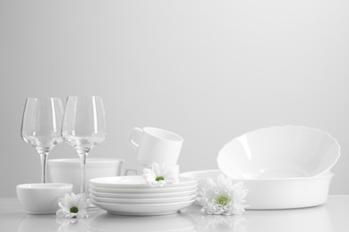 Photo of Set of many clean dishware, flowers and glasses on light table. Space for text