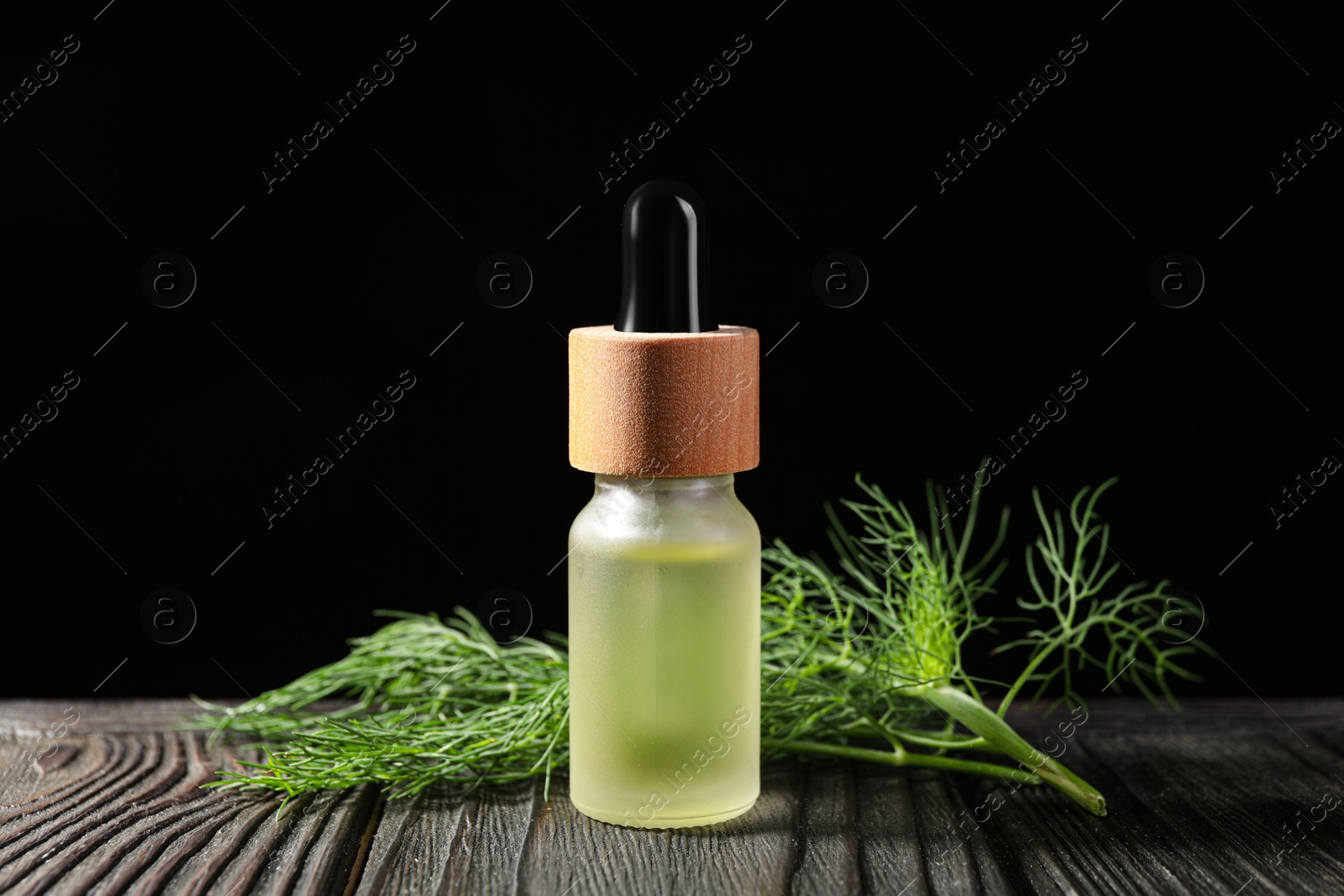 Photo of Bottle of essential oil and fresh dill on dark wooden table against black background, closeup