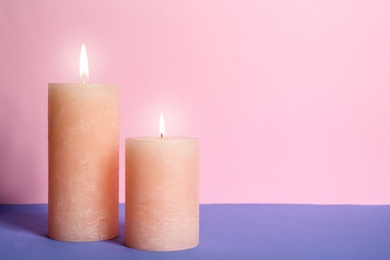 Photo of Decorative wax candles on table against color background