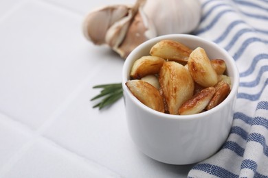 Photo of Fried garlic cloves in bowl on white table, closeup. Space for text