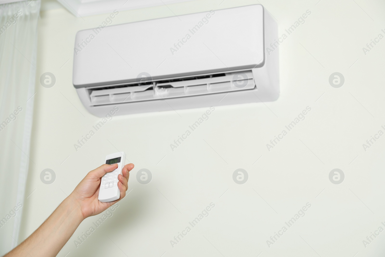 Photo of Man operating air conditioner with remote control indoors, closeup