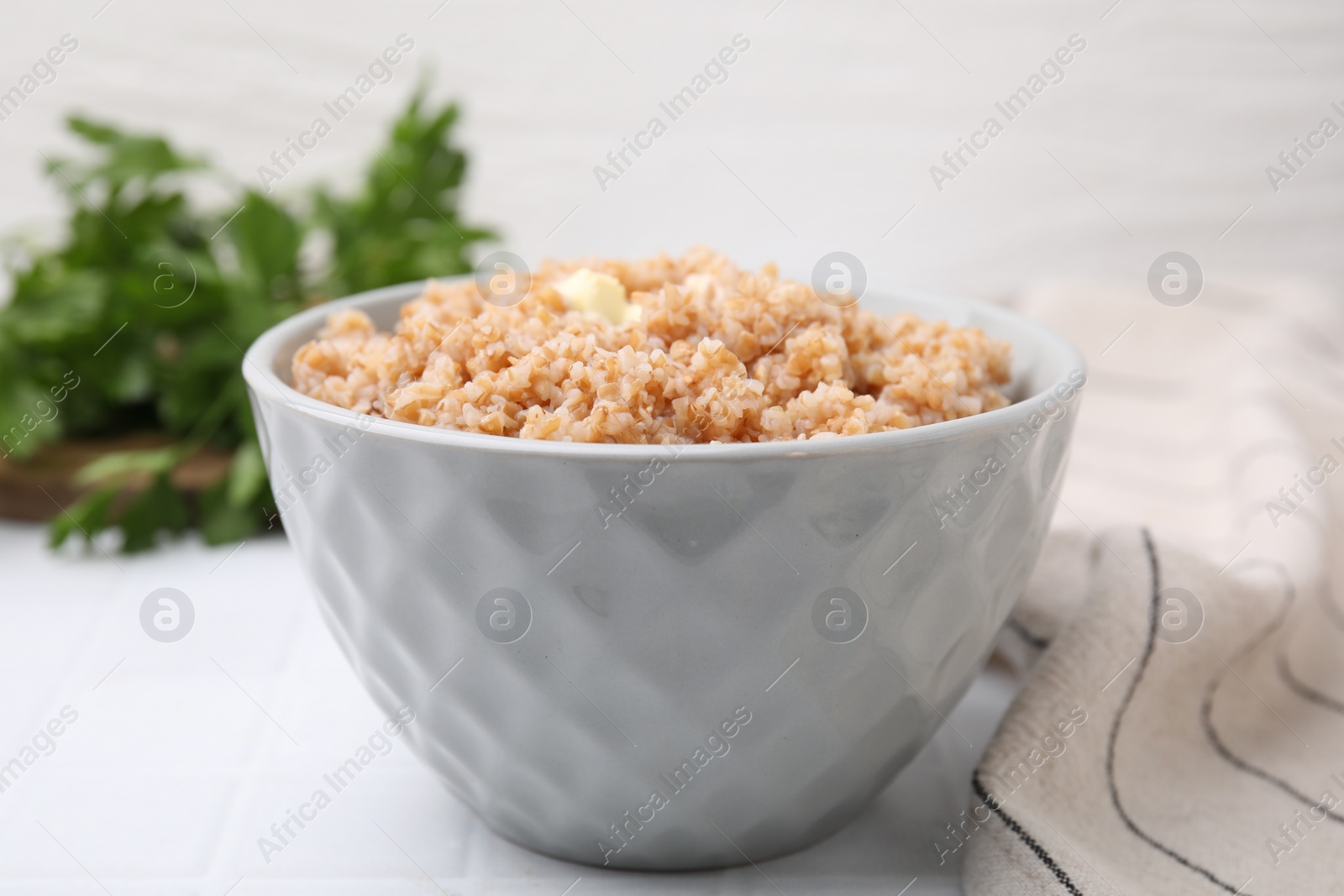 Photo of Tasty wheat porridge with butter in bowl on white tiled table, closeup