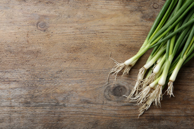 Photo of Fresh green spring onions on wooden table, flat lay. Space for text