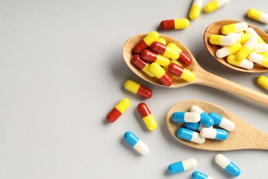 Photo of Many antibiotic pills with wooden spoons and space for text on grey background, top view. Medicinal treatment