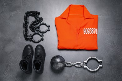Photo of Prisoner ball with chain, jail clothes and boots on grey table, flat lay