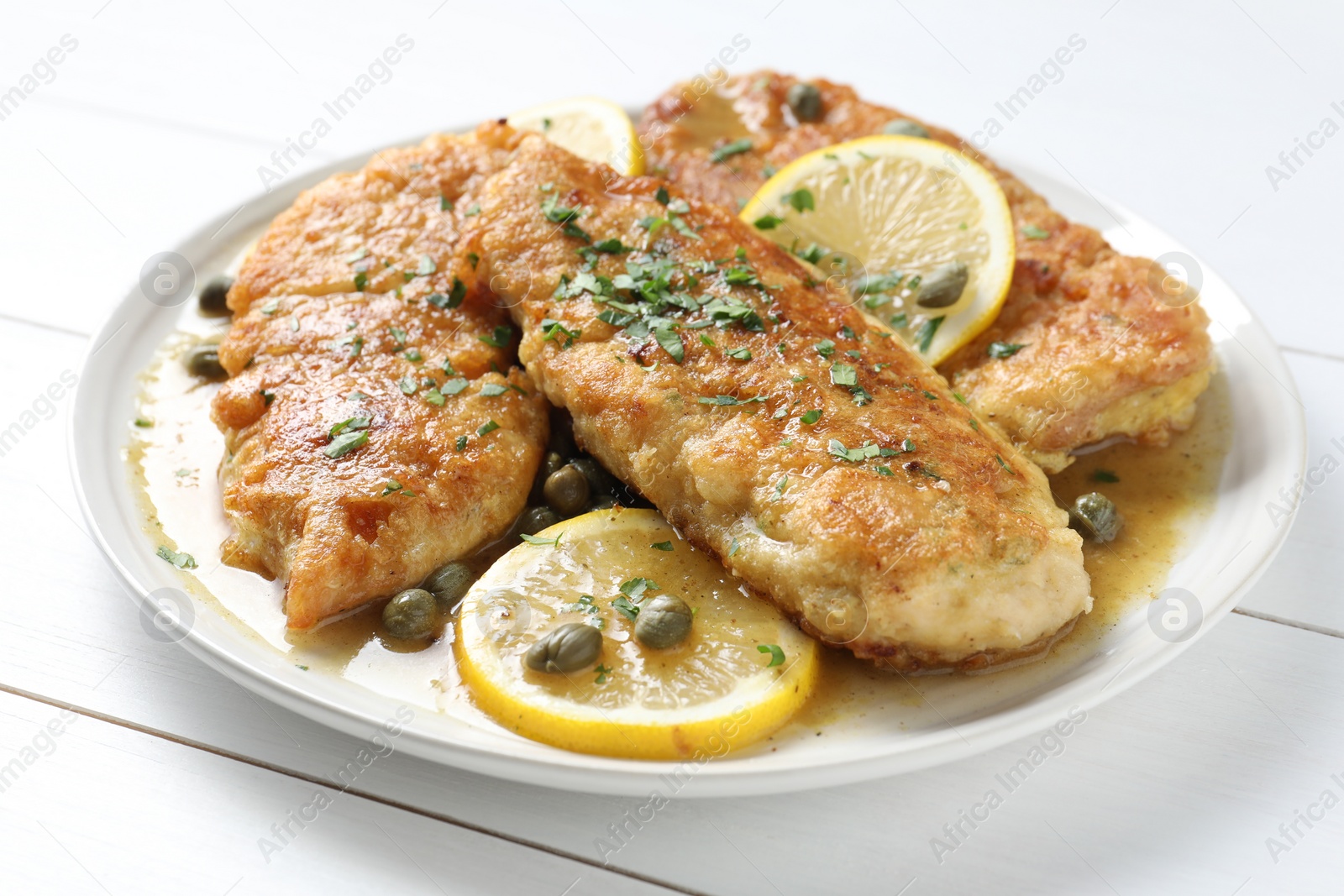 Photo of Delicious chicken piccata on white wooden table, closeup