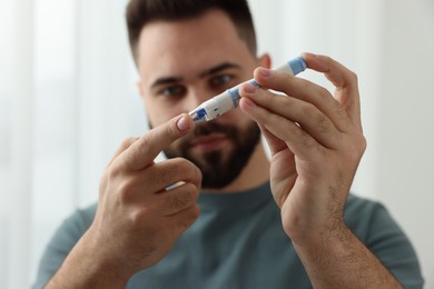 Photo of Diabetes test. Man checking blood sugar level with lancet pen at home, selective focus