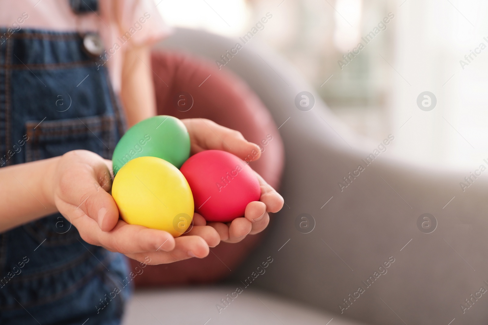 Photo of Little girl holding Easter eggs indoors, closeup. Space for text