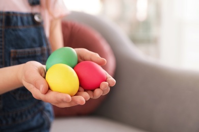 Photo of Little girl holding Easter eggs indoors, closeup. Space for text