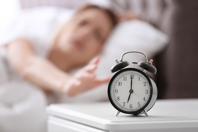 Photo of Alarm clock on table and woman in bedroom. Sleeping time