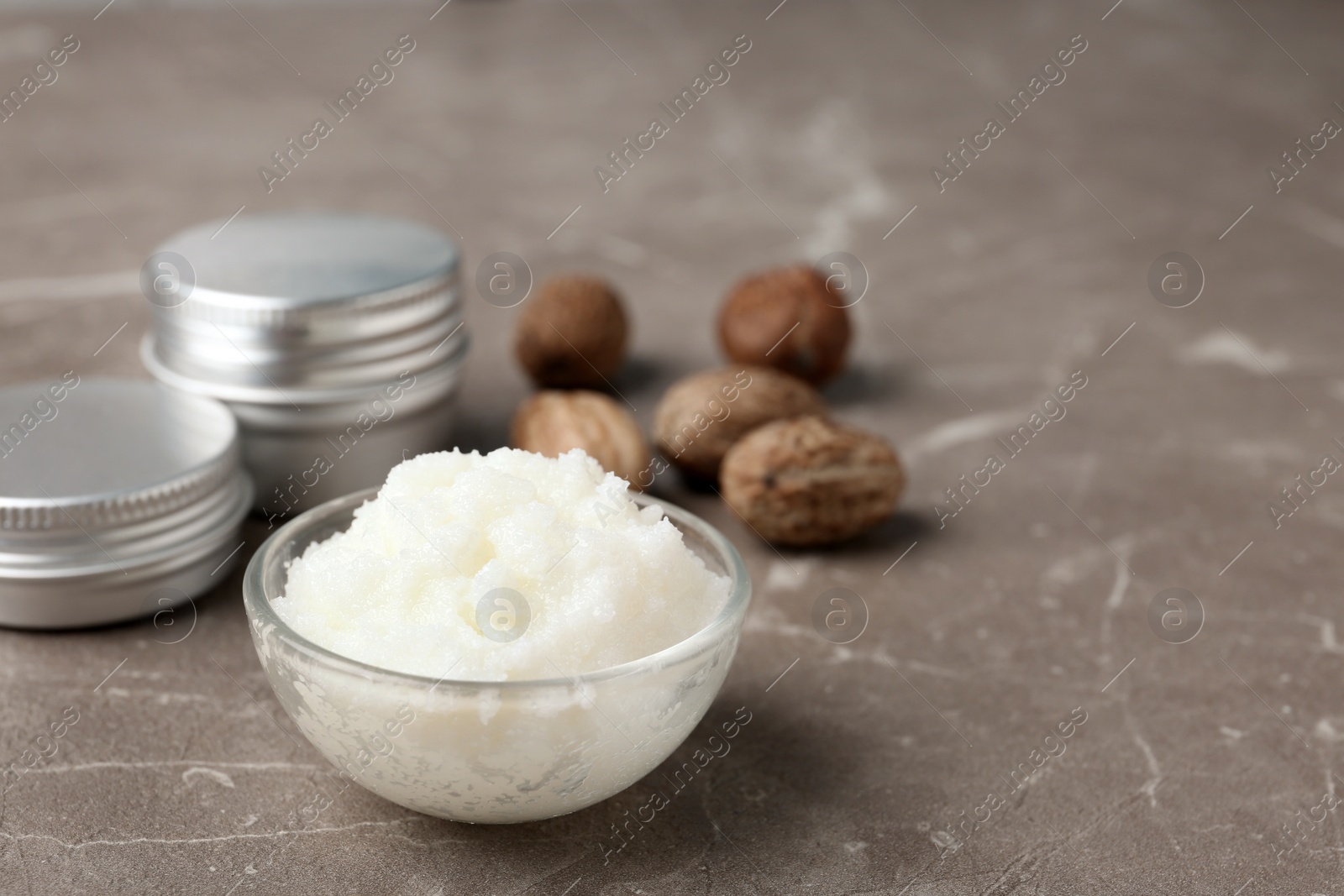 Photo of Shea butter in bowl and nuts on grey background. Space for text