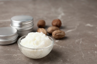 Shea butter in bowl and nuts on grey background. Space for text