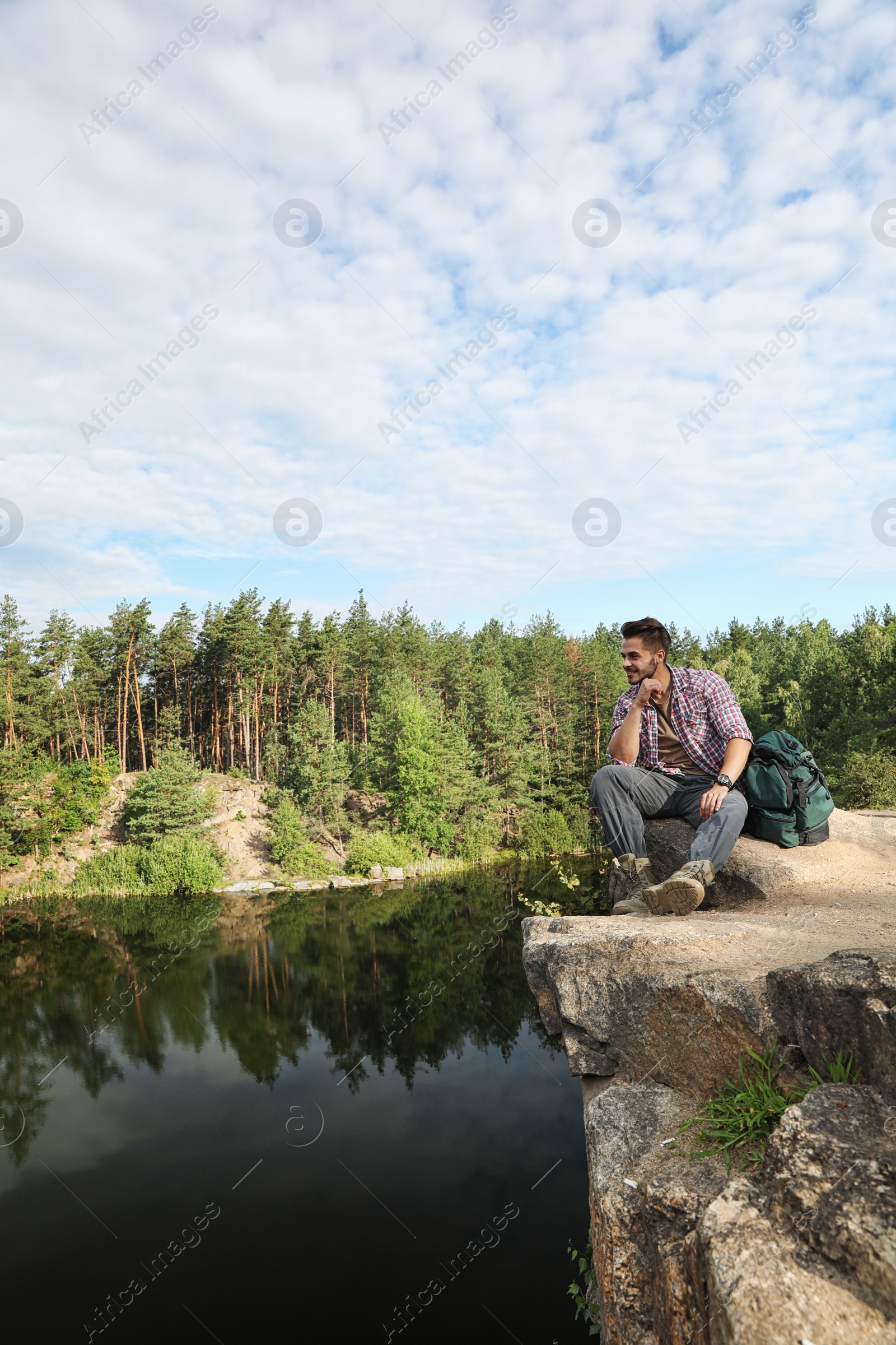 Photo of Young man on rock near lake and forest. Camping season