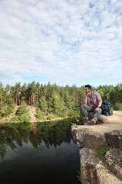 Young man on rock near lake and forest. Camping season