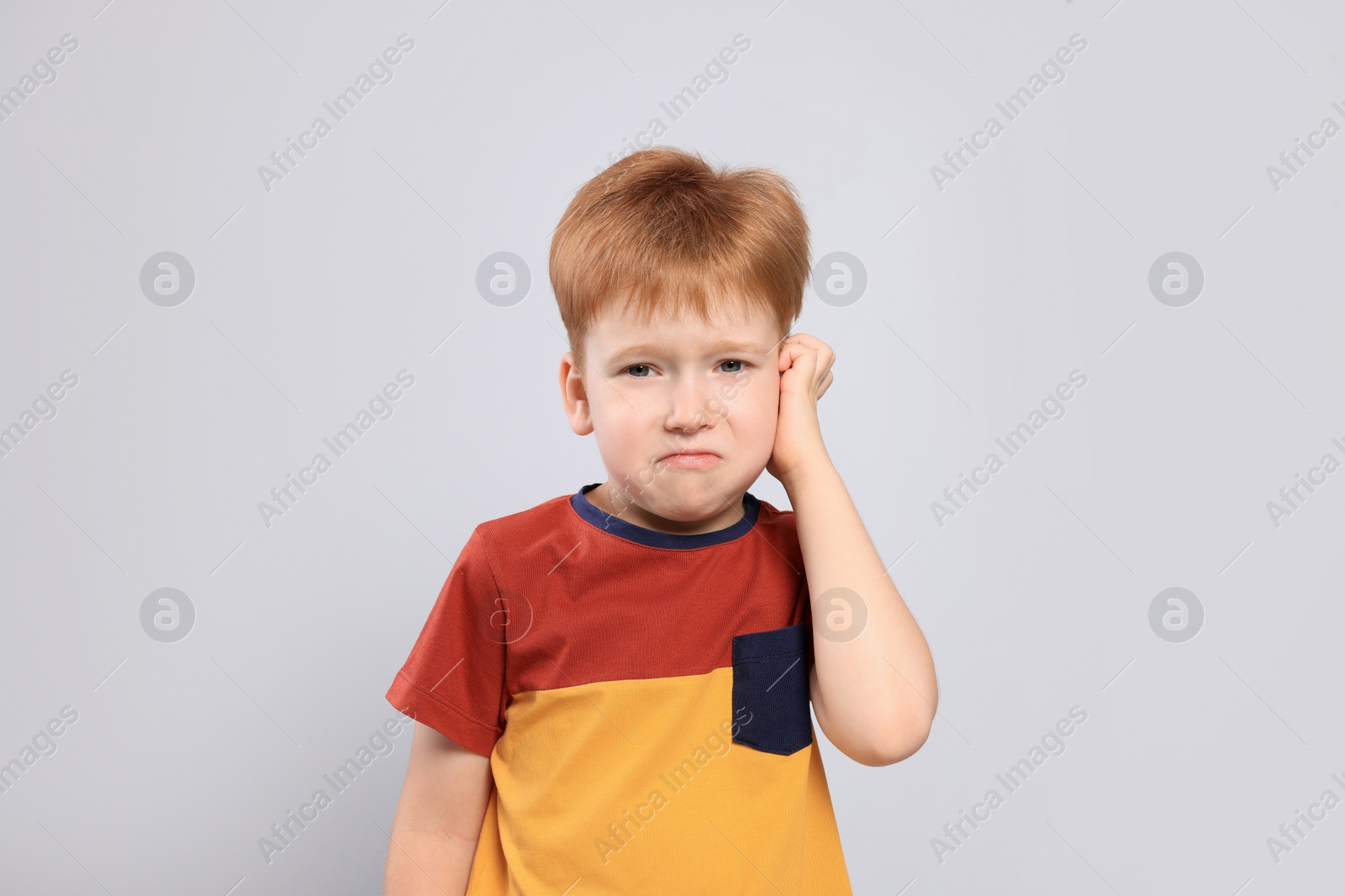 Photo of Little boy suffering from ear pain on light grey background