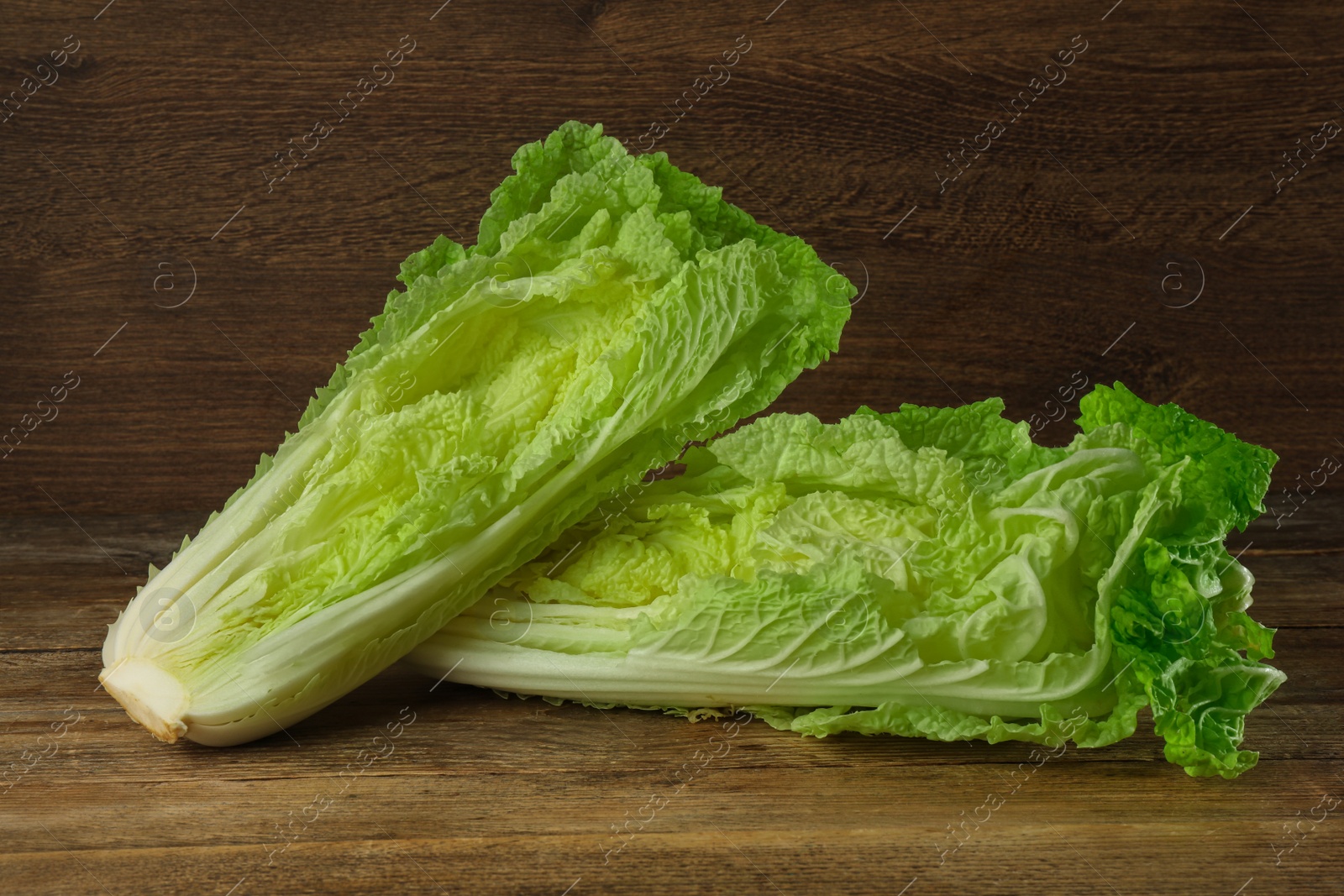 Photo of Cut fresh ripe Chinese cabbages on table against wooden background