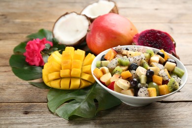 Delicious exotic fruit salad and ingredients on wooden table