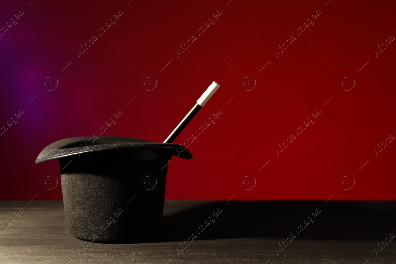 Photo of Magician's hat and wand on black wooden table against color background, space for text