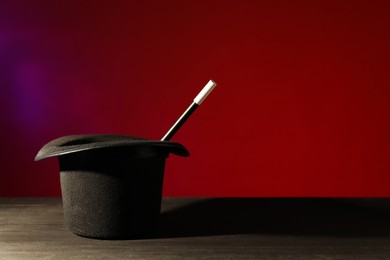 Photo of Magician's hat and wand on black wooden table against color background, space for text