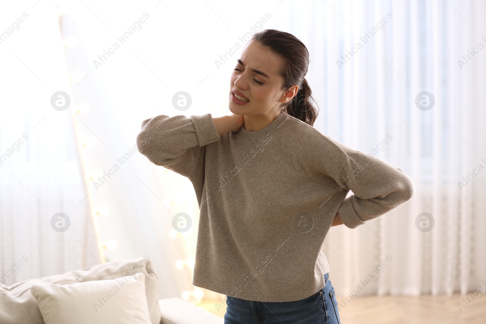 Photo of Woman suffering from back pain at home. Bad posture problem