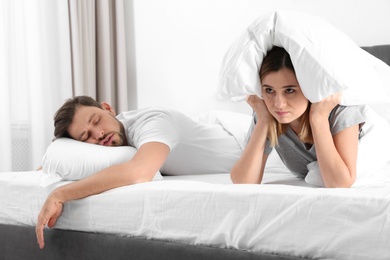 Photo of Upset woman covering her head with pillow near sleeping husband in bedroom. Relationship problems