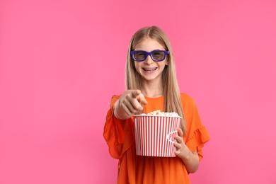 Teenage girl with 3D glasses and popcorn during cinema show on color background