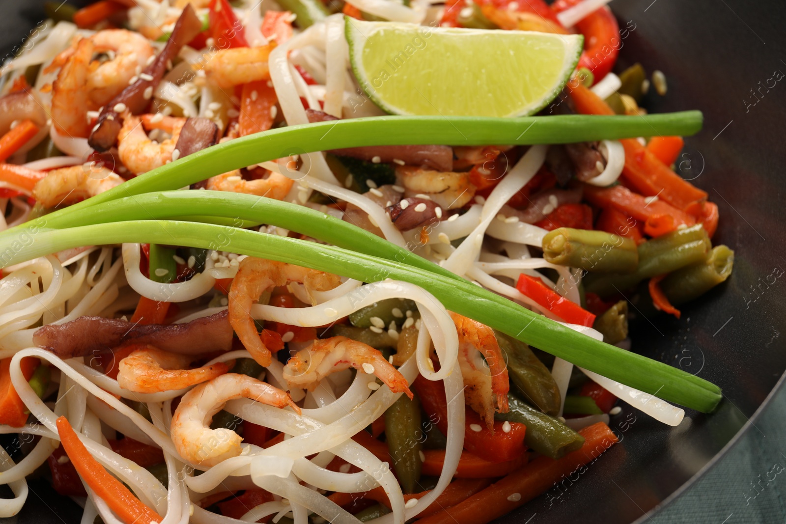 Photo of Shrimp stir fry with noodles and vegetables in wok on table, closeup