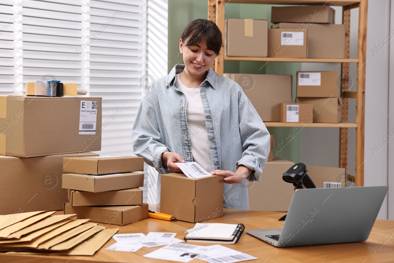 Photo of Parcel packing. Post office worker sticking barcode on box at wooden table indoors