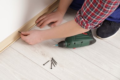 Man installing plinth on laminated floor in room, closeup