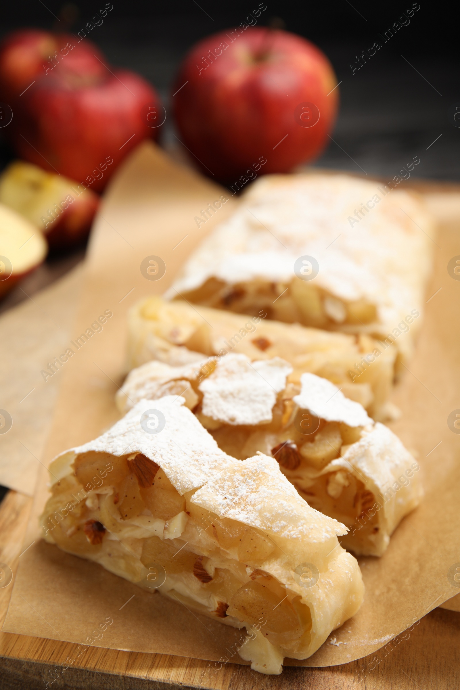 Photo of Delicious apple strudel with almonds and powdered sugar on parchment, closeup