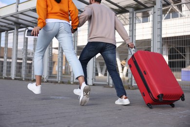 Photo of Being late. Couple with red suitcase running outdoors, closeup