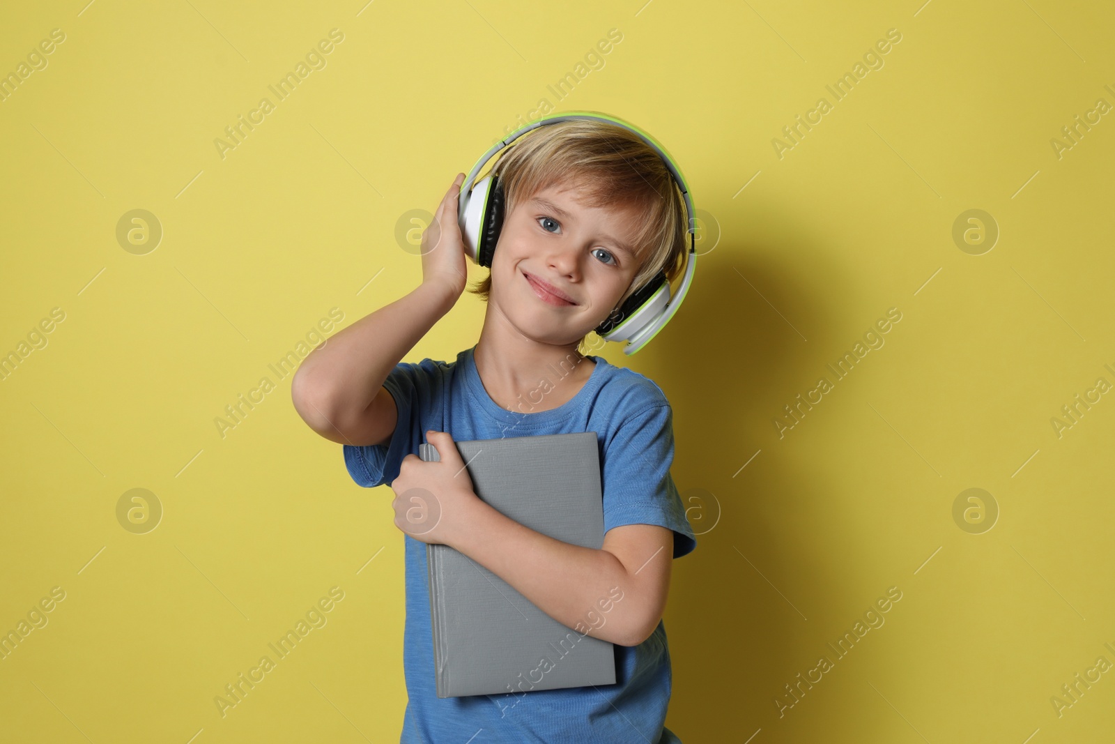 Photo of Cute little boy with headphones listening to audiobook on yellow background