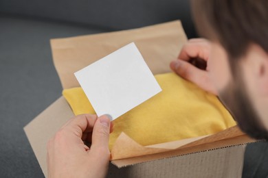 Photo of Man holding greeting card near parcel with Christmas gift, closeup